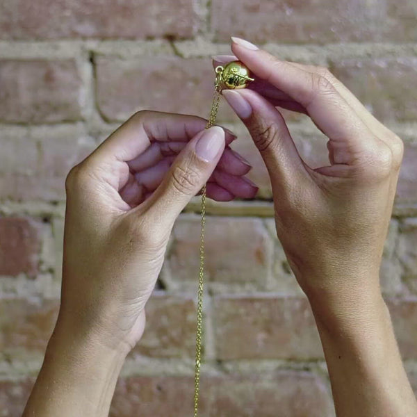 Video shows hands opening the gold Sphere + Wand necklace.