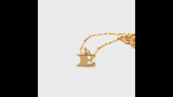 Video shows a 360 video of the E letter necklace. The 'E' pendant is the main focus and the video shows the wave detailing on the back. Next to the 'E' letter pendant is the gold twisted bar chain.