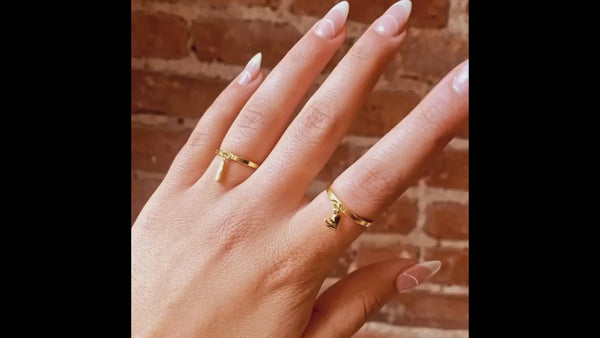 Image shows two gold charm rings worn by a model. She is waving her fingers. The charm rings worn are the gold Bandaid Charm Ring and the Mending Heart Charm Ring.