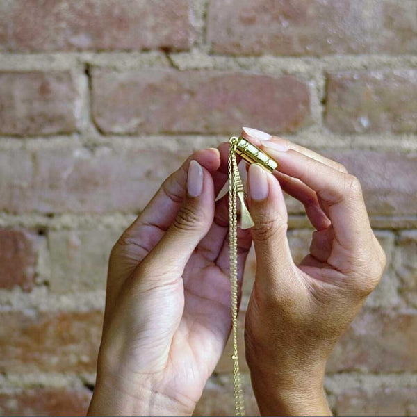 A video of two hands showcasing our gold capsule and wand necklace in front of a brick wall.
